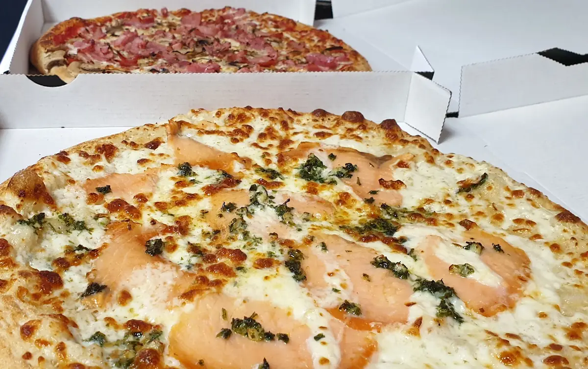 Une pizza au saumon et une pizza au jambon dans leurs boîtes